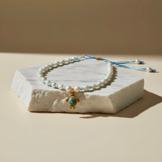 Embrace the serene beauty of the sea with the Cerulean Voyager adjustable necklace, combining light blue shell rondelles with lustrous freshwater pearls, finished with a charming stainless steel tortoise pendant.