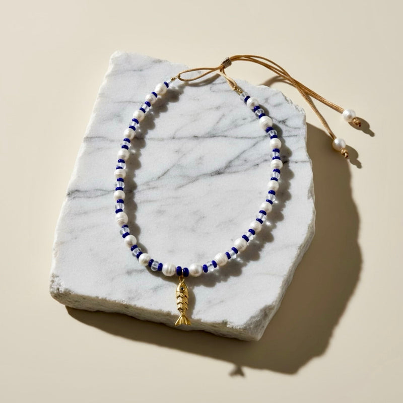 Dive into the Blue Lagoon, a serene blend of freshwater pearls, sparkling clear beads, and vibrant royal blue accents that inspire confidence and tranquility. A stainless steel fish pendant adds a marine touch and represents adaptability and the flow of life.