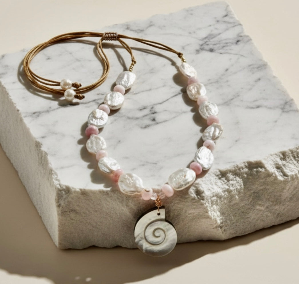 Ocean Muse – Blush is a delicate tribute to the quiet poetry of the sea at sunrise. This ethereal necklace features luminous baroque pearls, each uniquely shaped to celebrate nature’s organic beauty, paired with soft blush opal rondelles that glow with gentle, rosy iridescence. At its heart rests a carved conch pendant in radiant mother-of-pearl, evoking the whispers of ocean tides and treasured coastal memories.