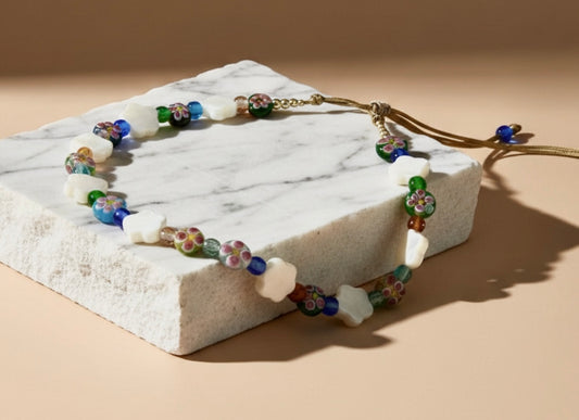 Ethereal and refined, Flowers of Nacre captures the quiet poetry of nature in bloom. Iridescent mother-of-pearl flowers glow with a soft, oceanic luster, intertwined with exquisite lampwork glass florals and radiant beads in a symphony of color.