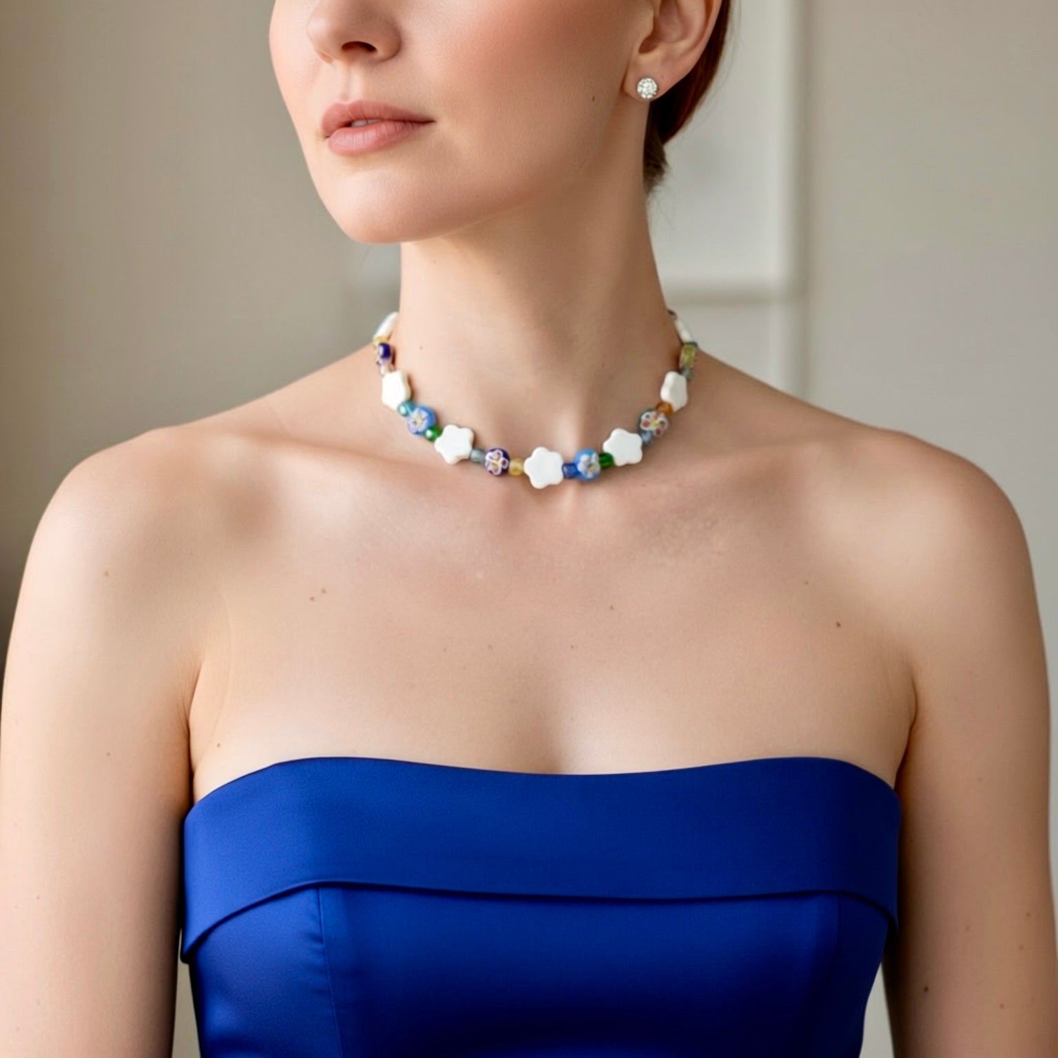 Woman wearing a blue strapless dress and a beaded necklace with a neutral background
